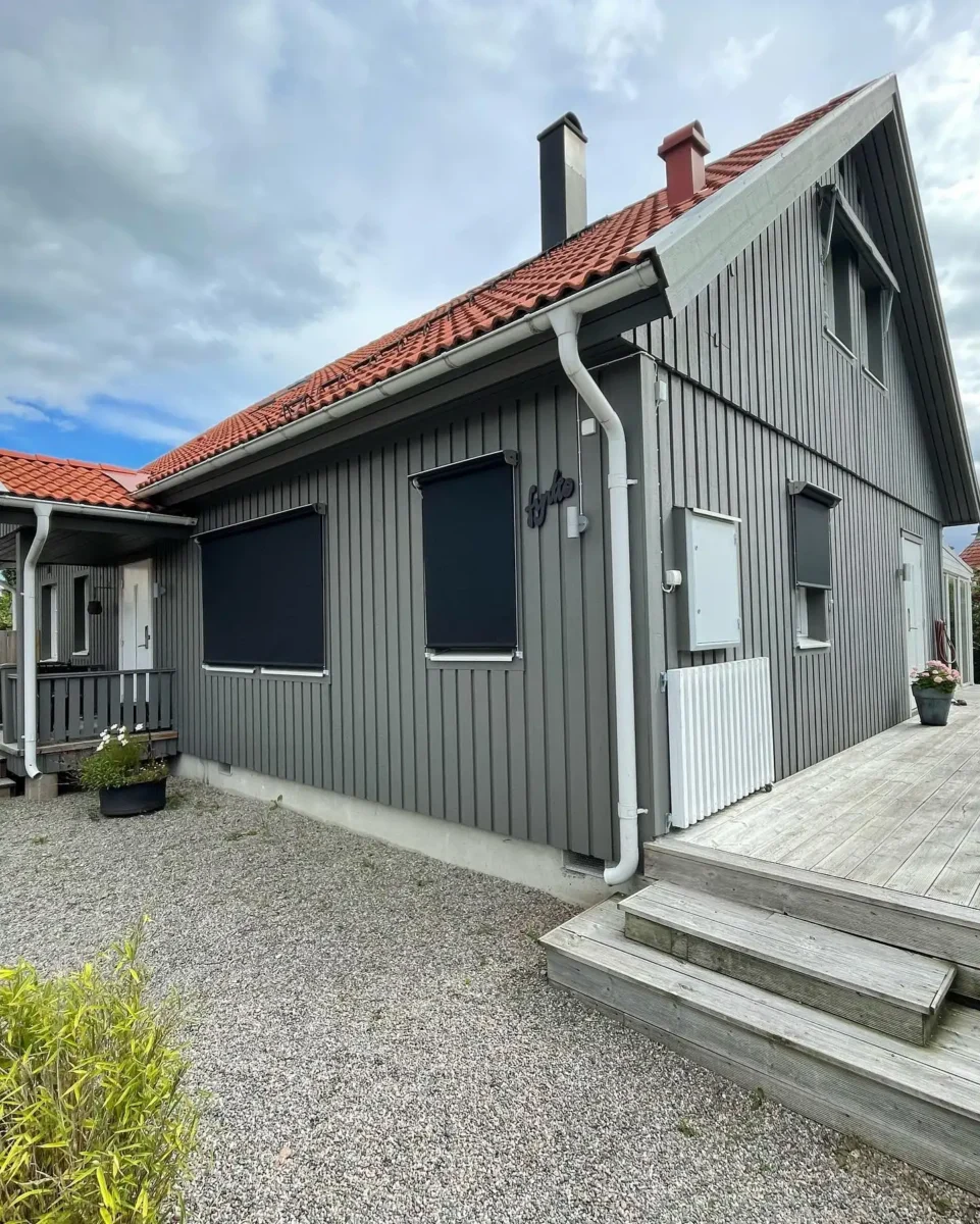 Grå trävilla med svarta zipscreens nedfällda för fönstren