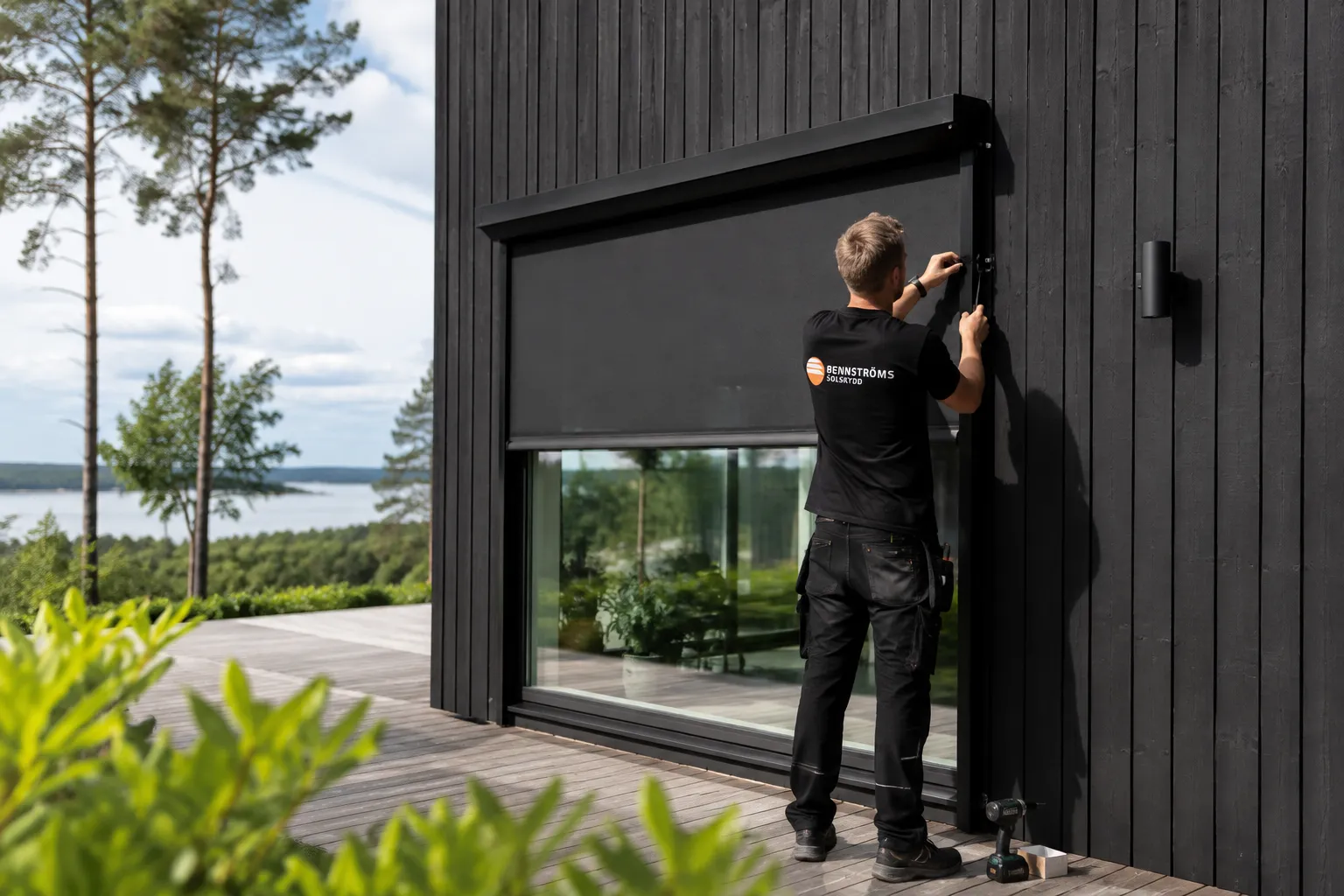 Montör från Bennströms monterar en svart zipscreen på en svart träfasad