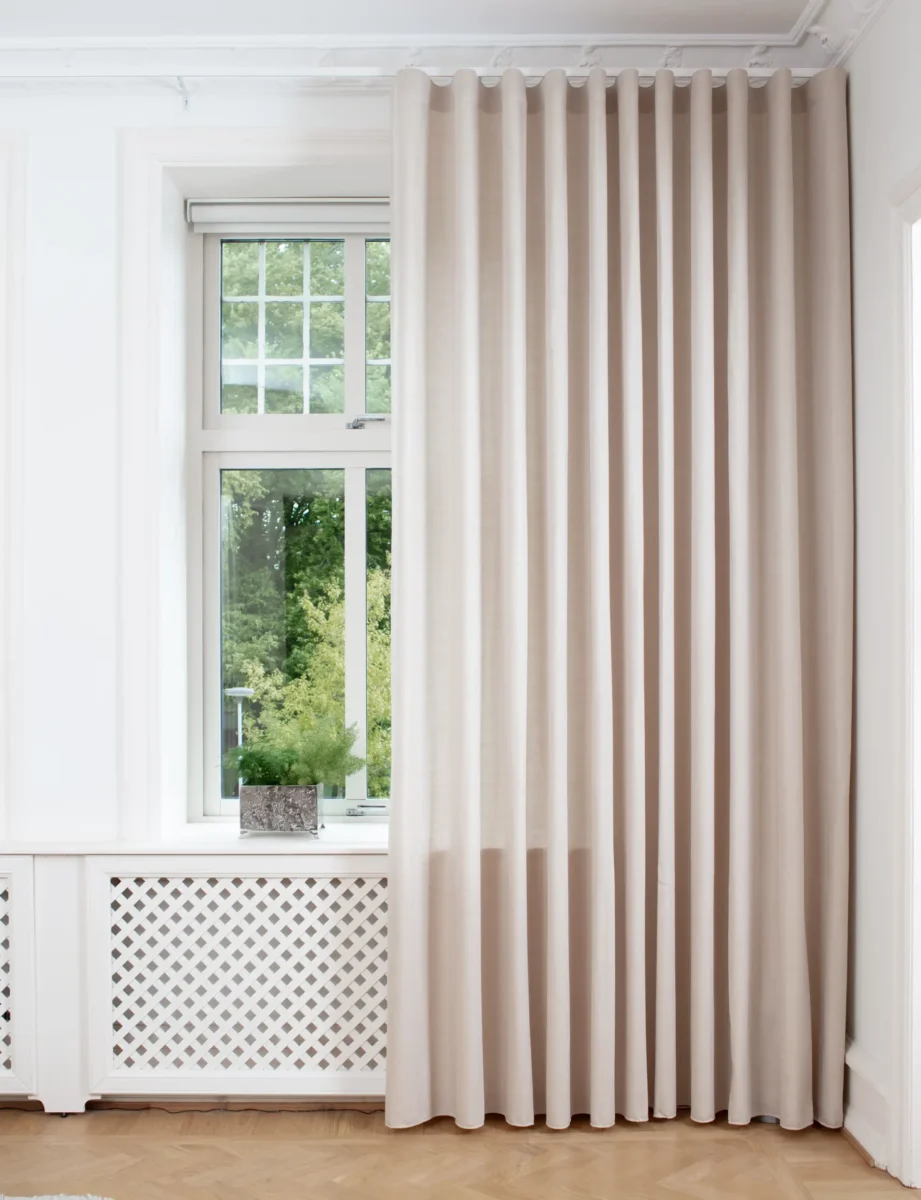 Ljusbeige gardiner från tak till golv bredvid ett spröjsat fönster