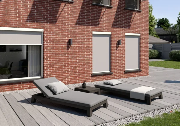 Grå zipscreens på en tegelvilla med solstolar på trädäcket framför