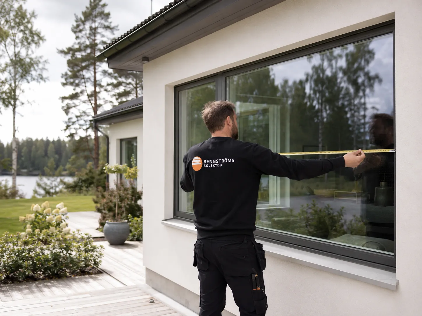 Montör från Bennströms mäter ett stort fönster med måttband på en vit villa