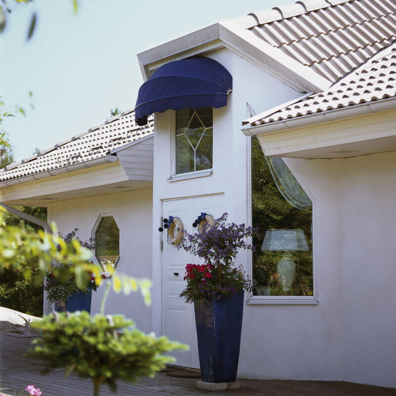 Mörkblå korgmarkis över ett fönster ovanför entrén på en vit villa