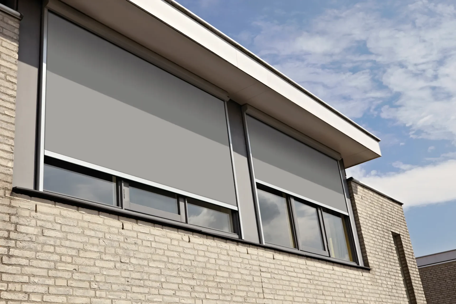Grå zipscreens nedfällda över en fönsterrad på en ljus tegelbyggnad