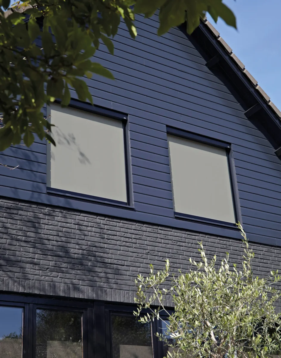 Grå zipscreens nedfällda för två fönster på en mörkblå träfasad