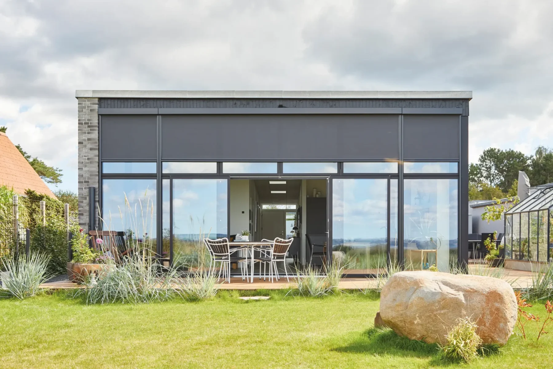 Villa med glasfasad där mörka zipscreens är halvvägs nedfällda