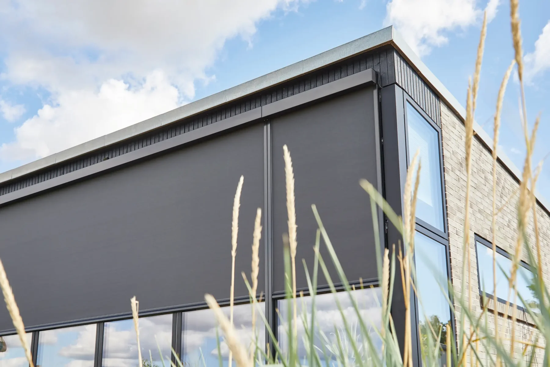 Närbild på mörka zipscreens nedfällda över glaspartierna på en modern villa