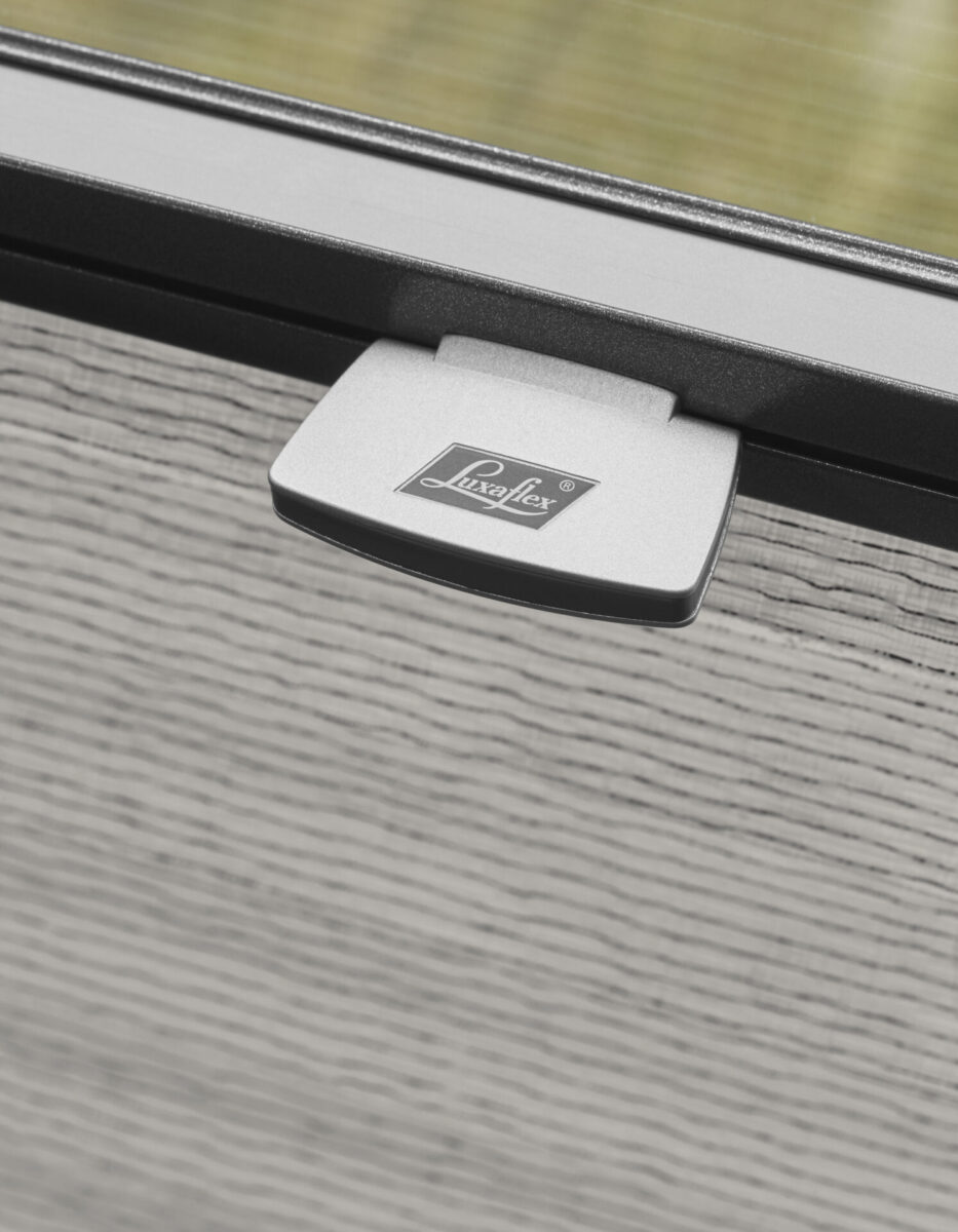 Närbild på handtaget med Luxaflex-logotyp på en grå plisségardin