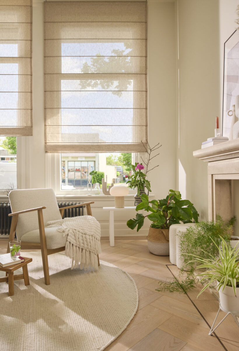Beige hissgardiner i höga fönster i ett ljust vardagsrum med gröna växter