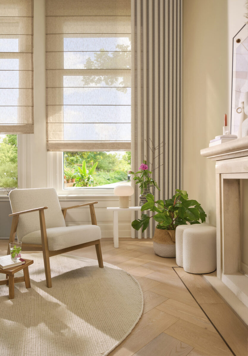 Beige hissgardiner i höga fönster vid en fåtölj med träram