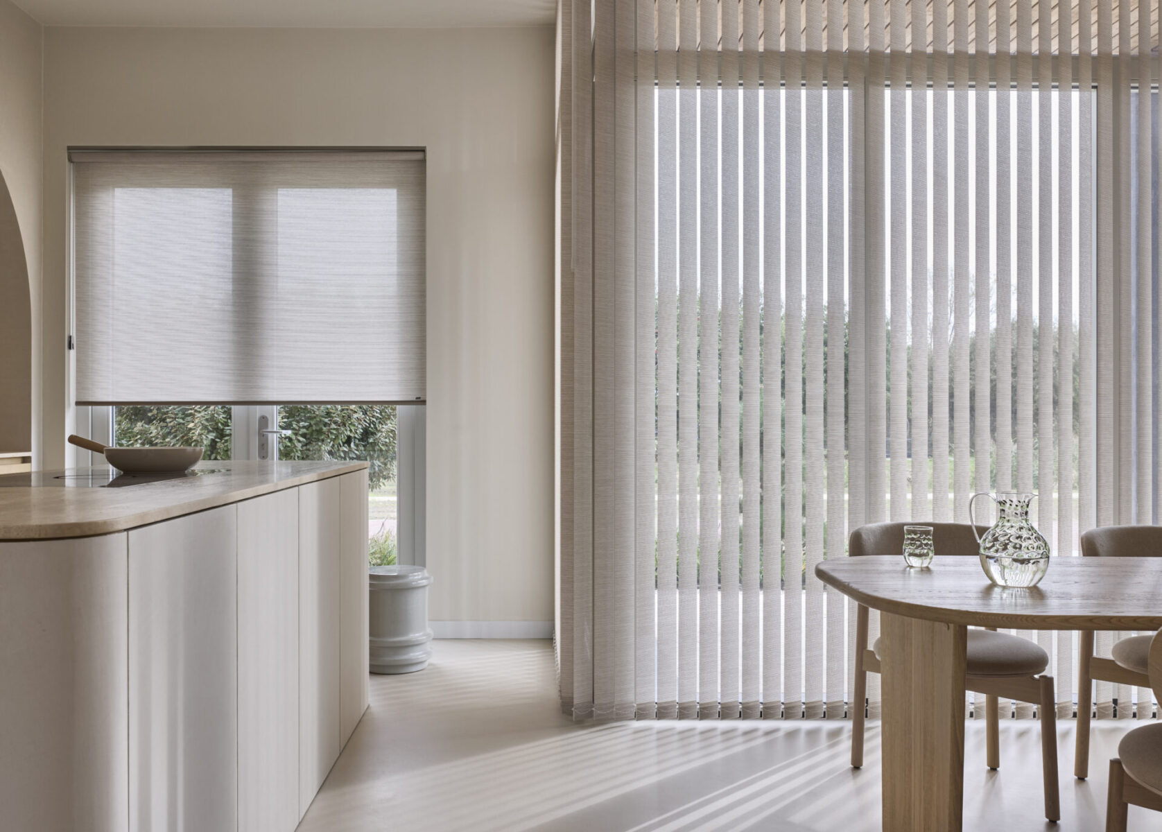 Beige lamellgardiner framför en glasdörr och en rullgardin i köksfönstret intill