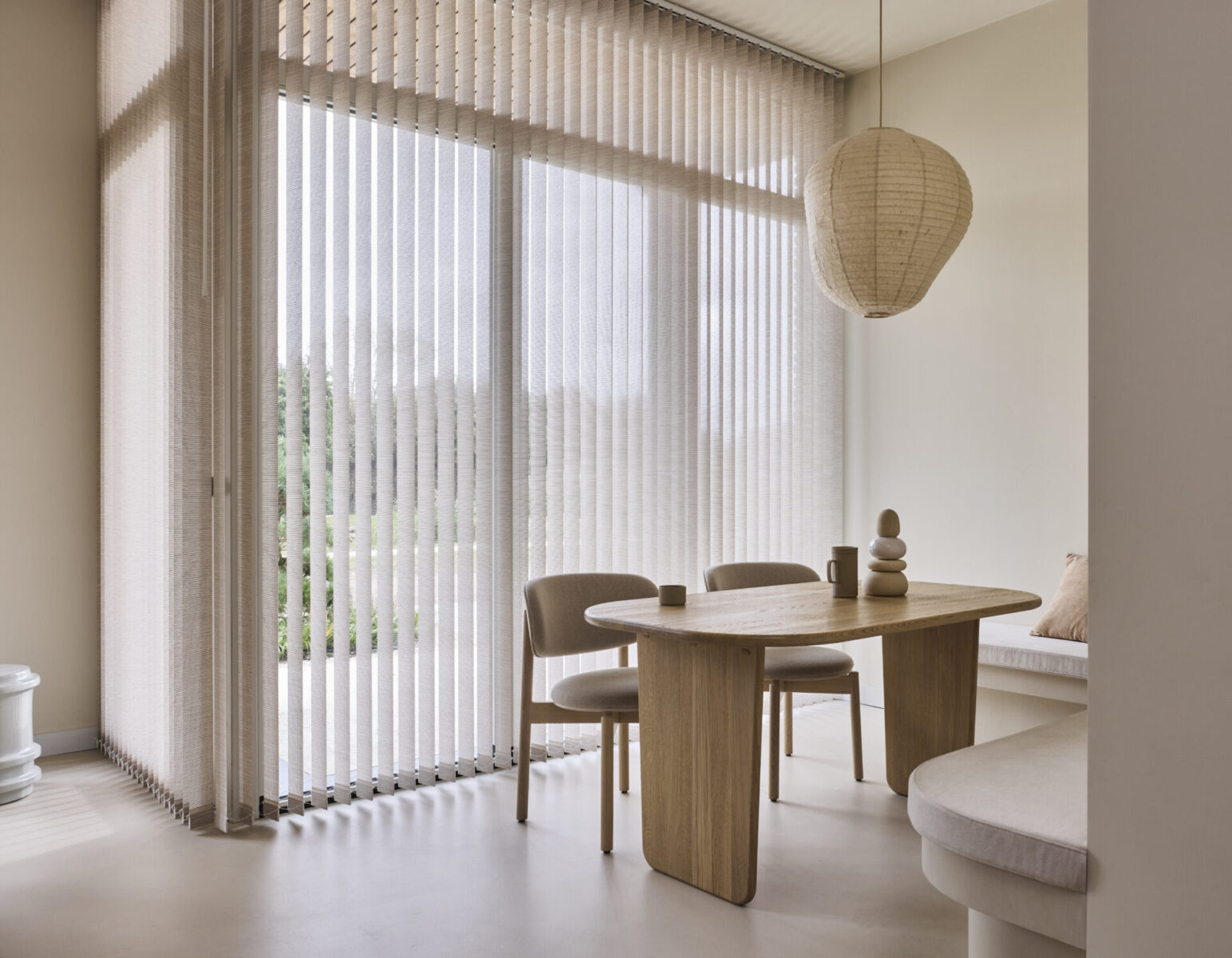 Beige lamellgardiner i höga fönster vid en matplats med rislampa